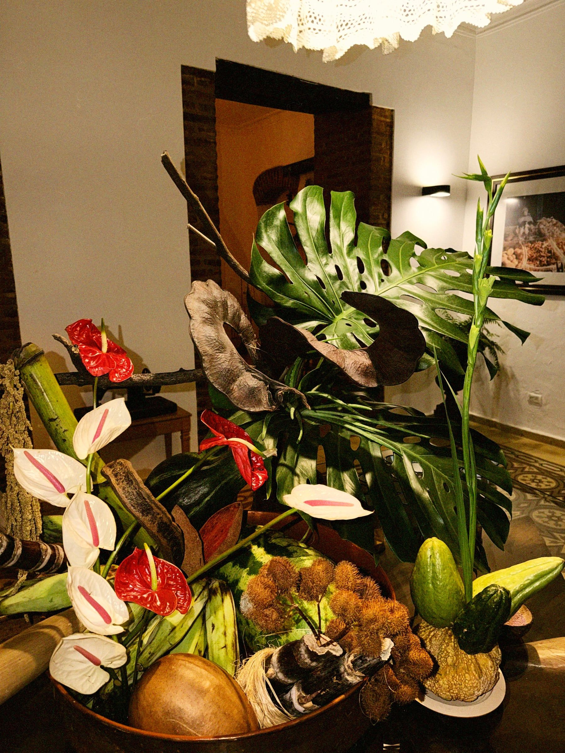 Centro de mesa con flores, hojas de monstera, frutos y vasijas de barro