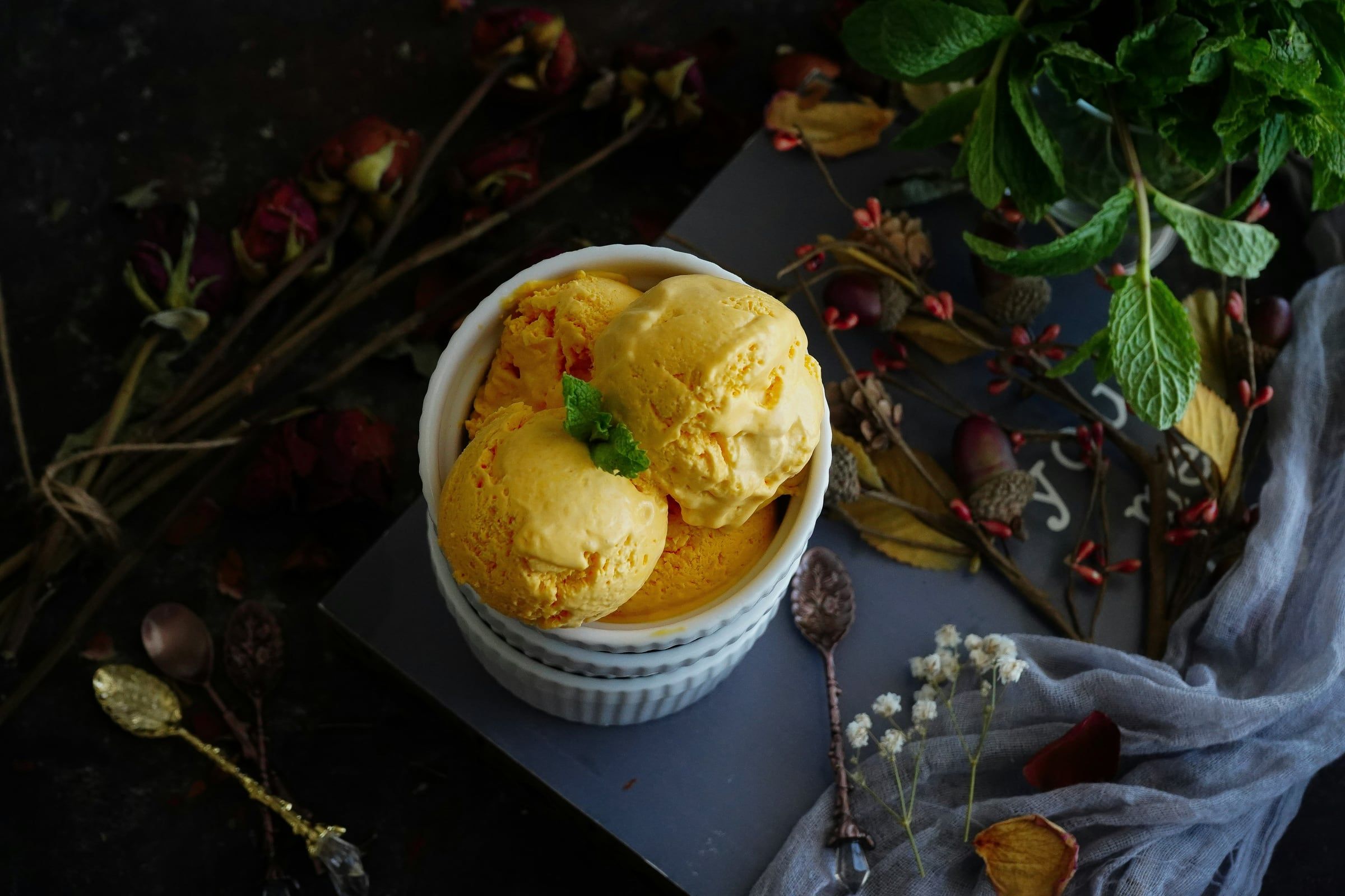 Bolas de helado de mango en un tazón blanco, entre hojas y flores
