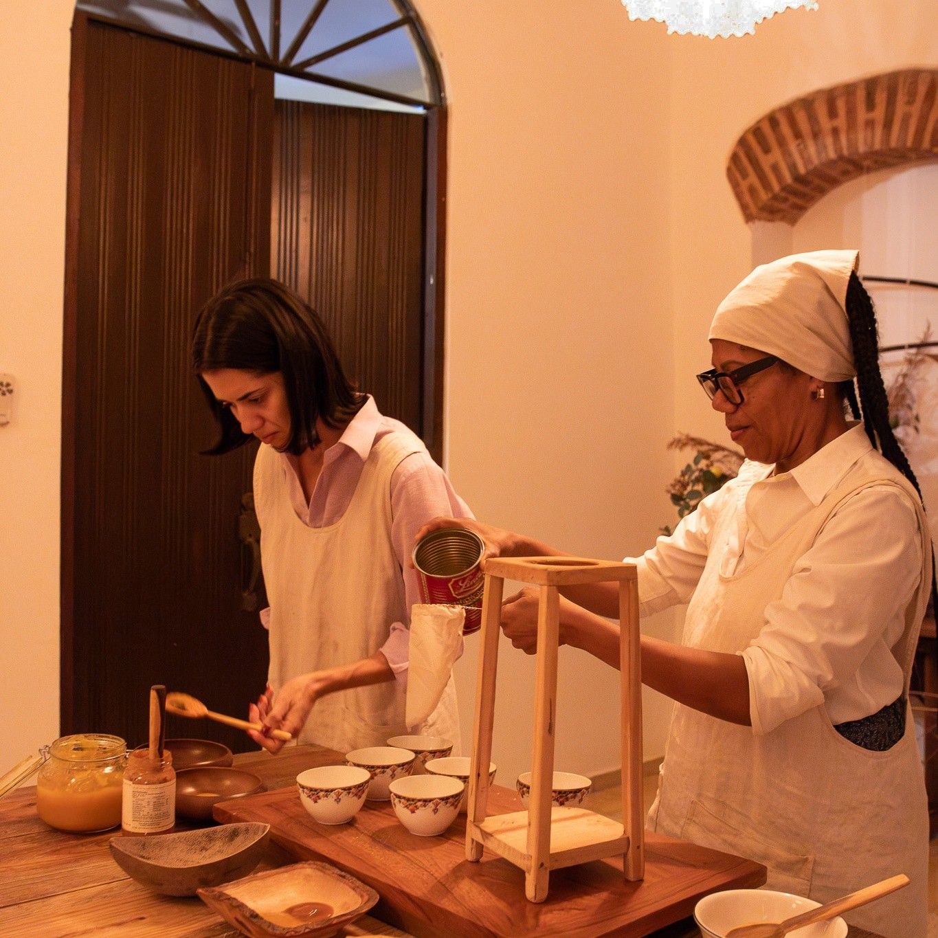 Giulia y Maribel preparan la mesa larga de la casa; Maribel cuela con un colador de tela sobre su soporte de madera