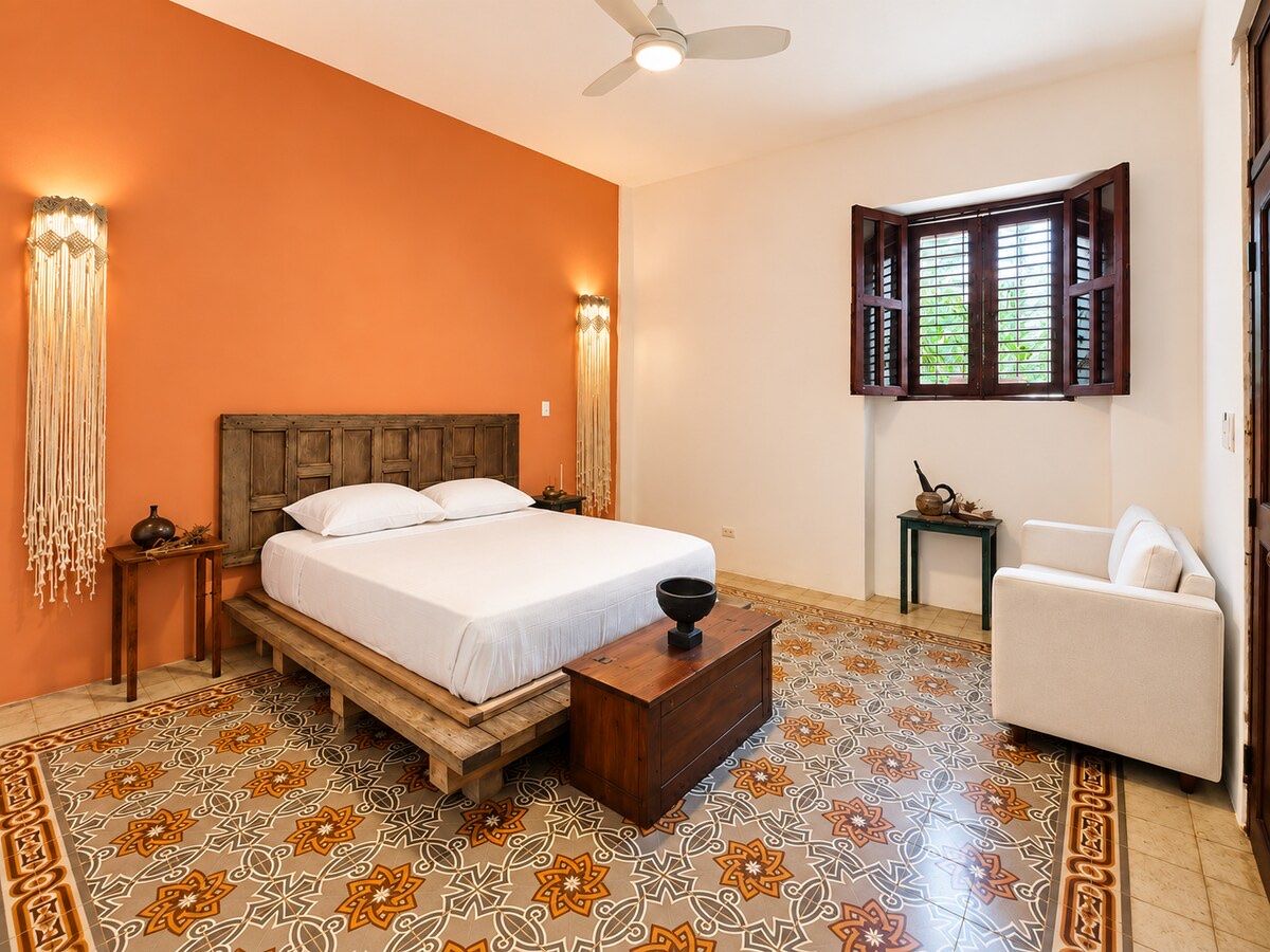 Una de las habitaciones, con la pared color terracota, cama de madera y piso de mosaico